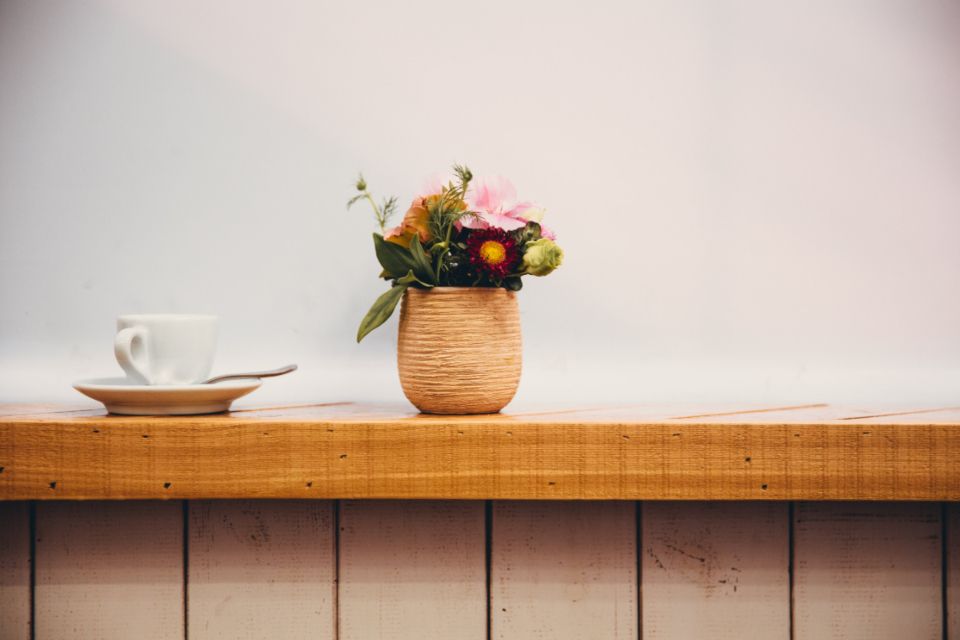 A coffee cup and a small vase of flowers on a sunny counter